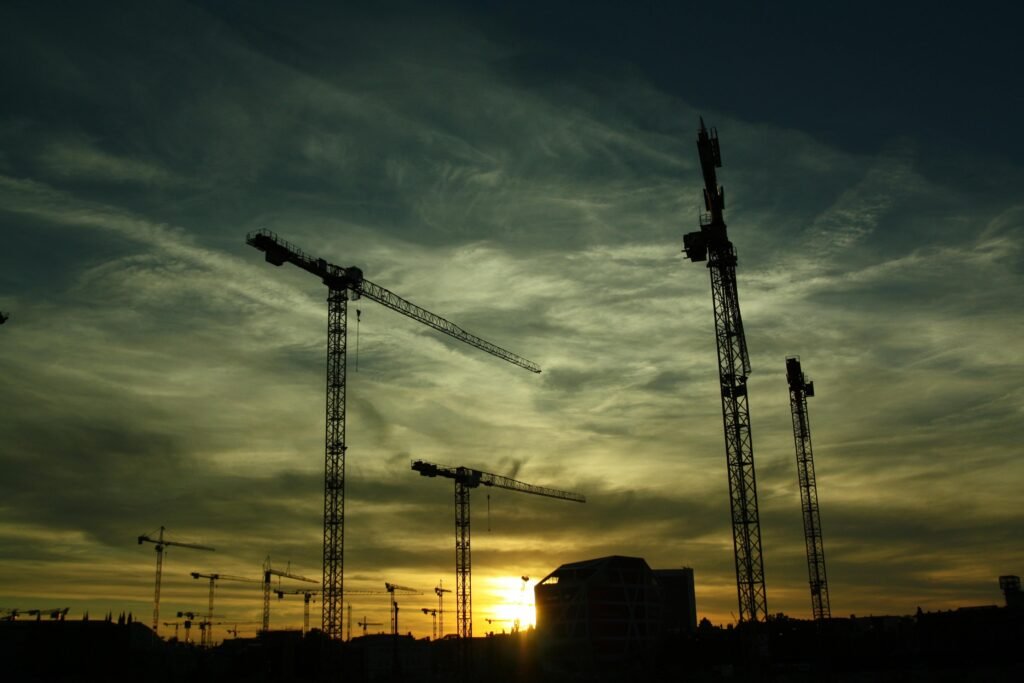 Silhouetted cranes at a construction site during sunset, showcasing industrial growth.
